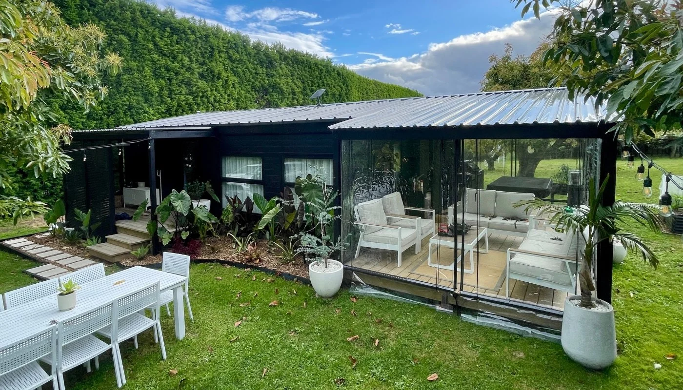 Dark charcoal prefab home with a timber deck in a palm clearing beside a turquoise lagoon